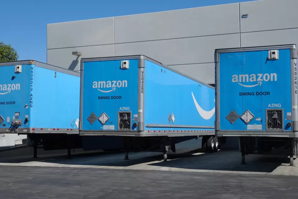 Three blue Amazon delivery trucks at bays at a distribution center